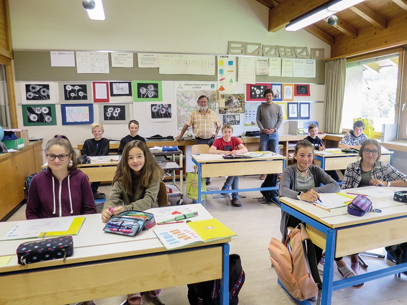 Die Klassenräume sind recht groß, die Schülerzahlen klein. So kann der Unterricht wie früher durchgeführt werden. Jeder Schüler teilt sich die Schulbank mit seinem Banknachbarn, ohne Maske. Hinten stehend: der Schulleiter und Lehrer Thomas Brülisauer (rechts) und der Lehrer der 6. Primarschulklasse Chasper Stuppan