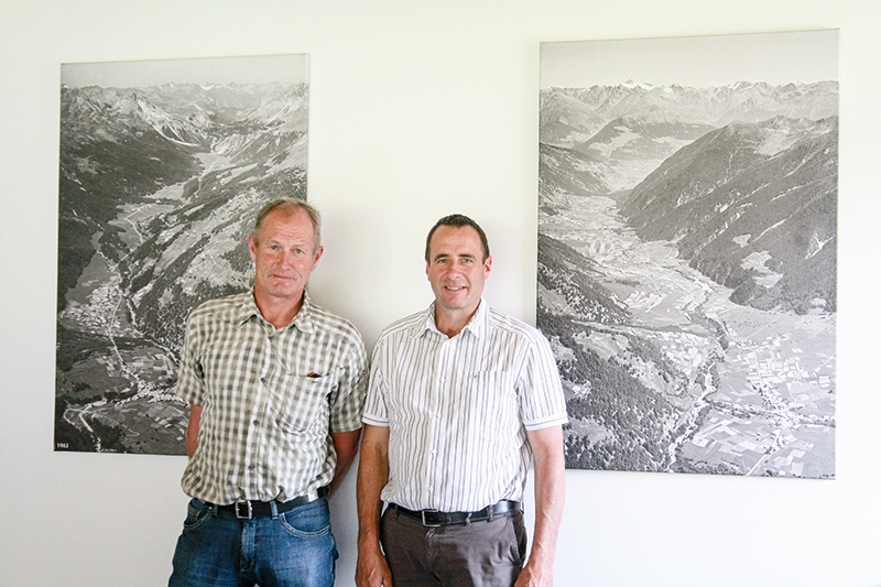 Der für Land- und Forstwirtschaft zuständige Gemeindevorstand Daniel Pitsch und der Gemeindepräsident der Gemeinde Val Müstair Rico Lamprecht: „Die Landwirtschaft ist die Basis für den Tourismus, für die Biosfera, für die Biodiversität und für die Kulturlandschaft.“ Im Hintergrund Bilder vom Val Müstair aus den 60er Jahren - viele Getreidefelder damals