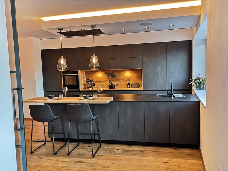 Realisiertes Projektbeispiel von Untermarzoner: grifflose Küche in geradlinigem Design. Die Fronten in Stahloptik elegant kombiniert mit warmen Akzenten in Eiche, ein Highlight die 15 mm Keramik-Platte
