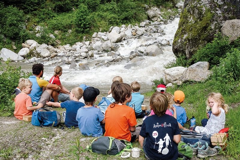 Die Kinder und Pädagogen/innen des Waldkindergartens Birkenwald in Partschins beim Jause-Essen am Ufer des Zielbachs