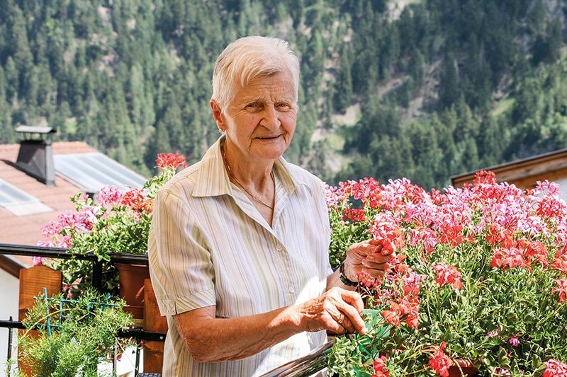 Margherita Rufinatscha Dietl, Jg. 1937, Taufers im Münstertal. Sie liebt ihre Blumen, ist humorvoll, gesellig und „hoangortet“ gerne. Ihre größte Freude ist es, wenn sich ihre Töchter, Schwiegersöhne, ihre zehn Enkel und ihre fünf Urenkel um sie herum scharen.